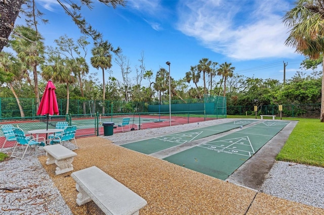 view of property's community featuring a tennis court, shuffleboard, and fence