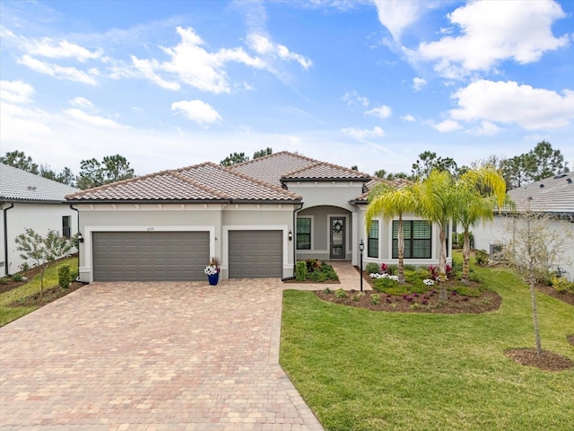 mediterranean / spanish-style home featuring a tiled roof, a front yard, stucco siding, decorative driveway, and an attached garage