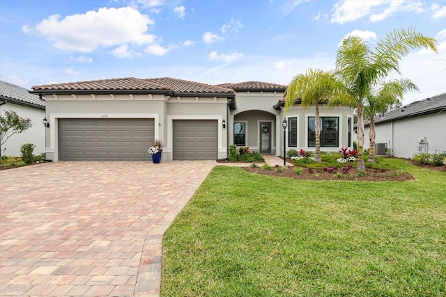 mediterranean / spanish-style home with stucco siding, a tile roof, decorative driveway, a front yard, and an attached garage