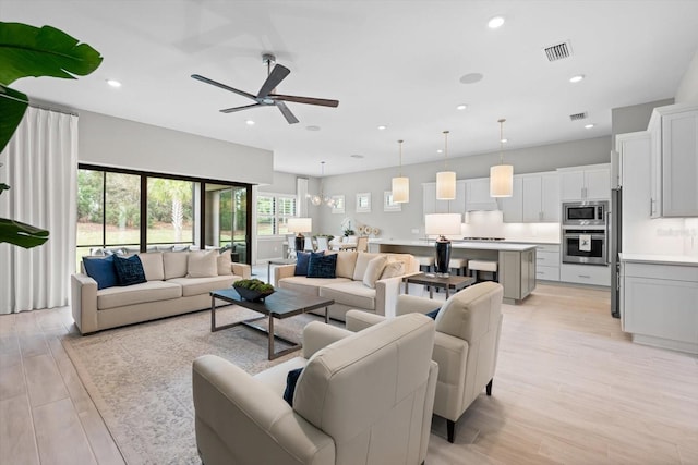 living area featuring ceiling fan with notable chandelier, light wood-style flooring, recessed lighting, and visible vents