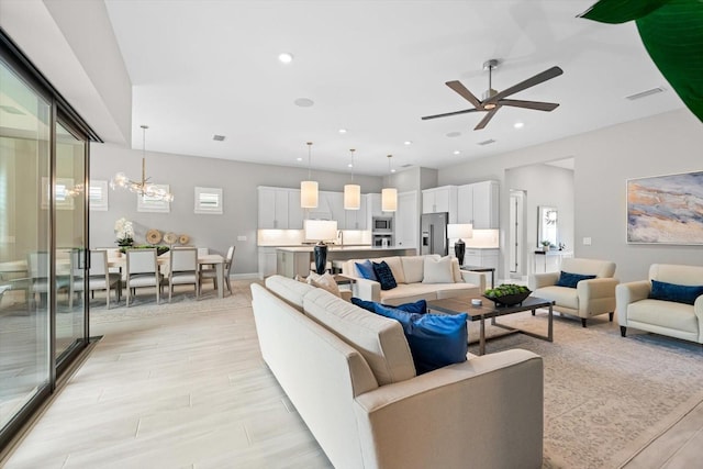 living room featuring ceiling fan with notable chandelier, recessed lighting, visible vents, and light wood finished floors