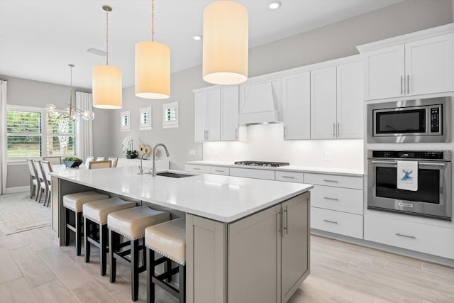 kitchen featuring an island with sink, a sink, stainless steel appliances, light countertops, and custom exhaust hood