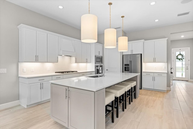 kitchen featuring a sink, stainless steel appliances, white cabinetry, and hanging light fixtures