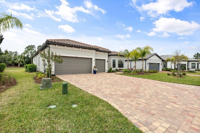 mediterranean / spanish house featuring stucco siding, decorative driveway, a front yard, an attached garage, and a tiled roof