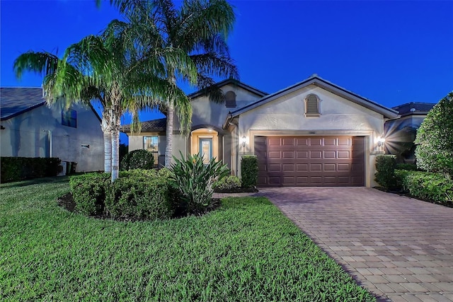 view of front of home featuring decorative driveway, an attached garage, a front yard, and stucco siding