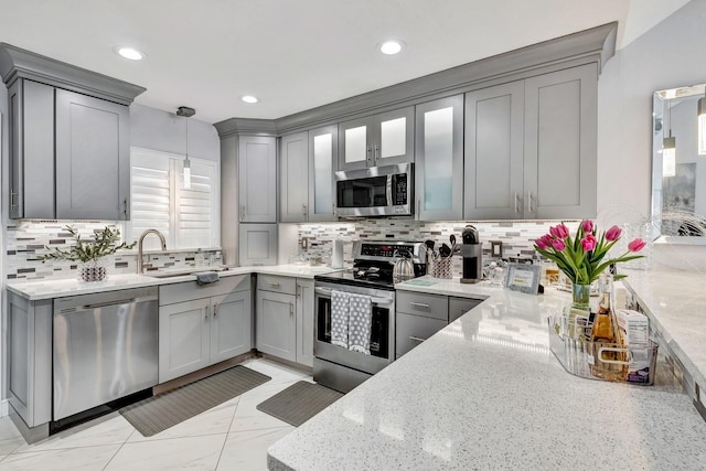 kitchen featuring light stone counters, decorative light fixtures, stainless steel appliances, gray cabinetry, and a sink