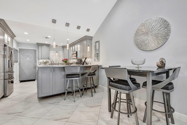 kitchen featuring a kitchen breakfast bar, a peninsula, marble finish floor, stainless steel appliances, and gray cabinetry