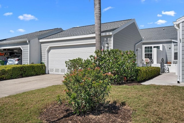 view of side of property featuring a garage, driveway, a shingled roof, and a yard