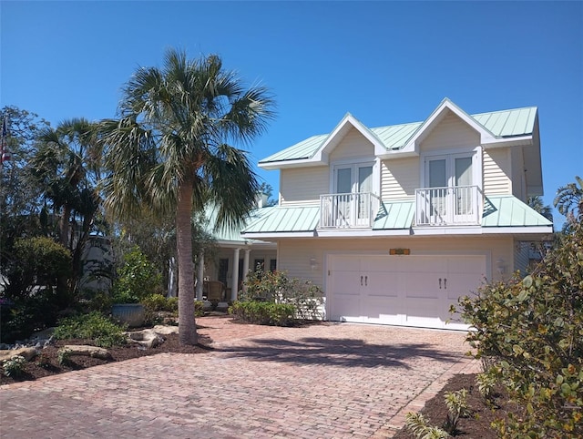 view of front of property with french doors, metal roof, decorative driveway, a balcony, and an attached garage