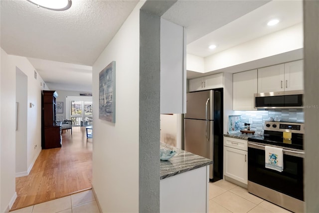 kitchen with white cabinets, stone countertops, stainless steel appliances, and backsplash