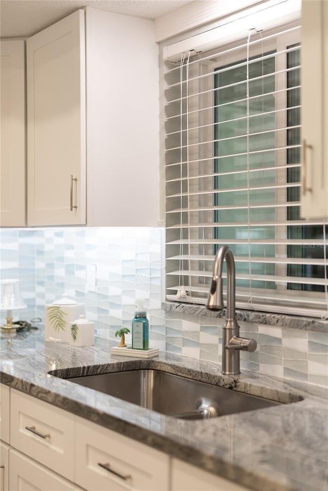 room details with light stone counters, tasteful backsplash, a sink, and white cabinetry