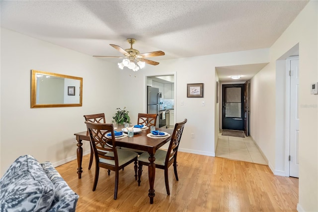 dining space featuring light wood-type flooring, ceiling fan, a textured ceiling, and baseboards