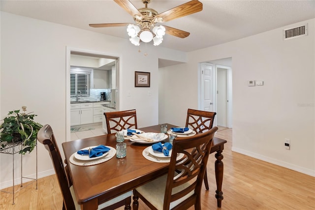 dining space with a ceiling fan, light wood-type flooring, visible vents, and baseboards