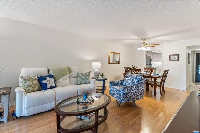 living room featuring light wood-style floors, ceiling fan, a textured ceiling, and baseboards