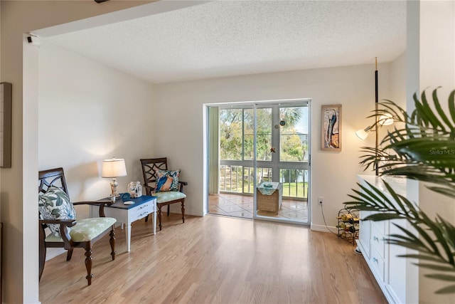 living area with baseboards, a textured ceiling, and light wood finished floors