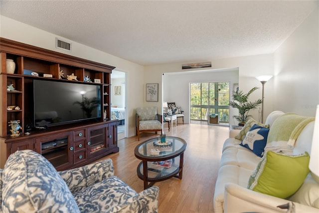 living room with visible vents, light wood-style flooring, and a textured ceiling