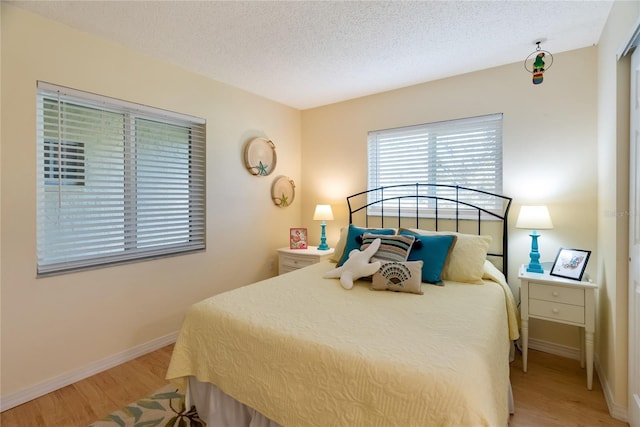 bedroom with light wood-type flooring, baseboards, and a textured ceiling