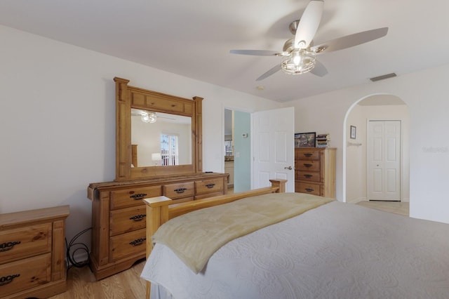 bedroom with light wood-style floors, arched walkways, visible vents, and ceiling fan