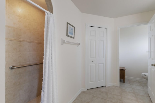 bathroom with baseboards, toilet, tile patterned floors, a tile shower, and a closet