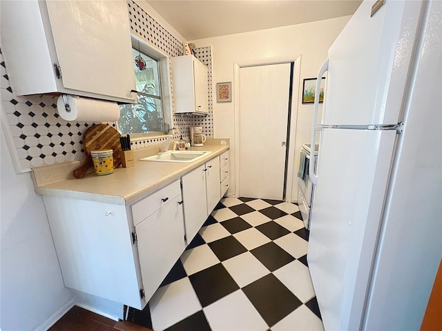 kitchen with freestanding refrigerator, a sink, light countertops, light floors, and backsplash