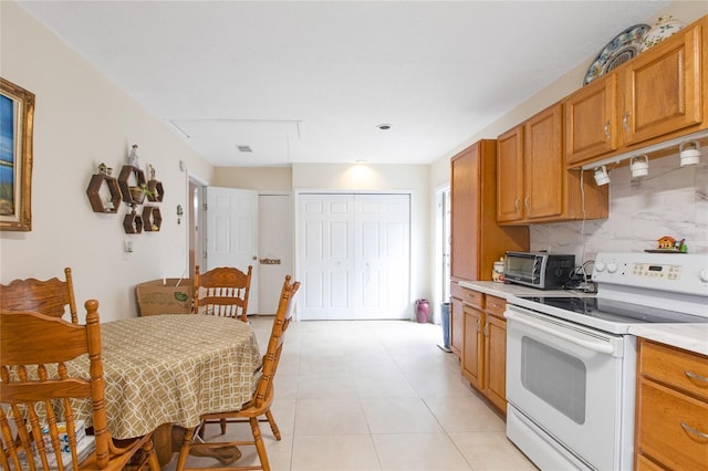 kitchen featuring white electric stove, a toaster, light countertops, tasteful backsplash, and brown cabinetry