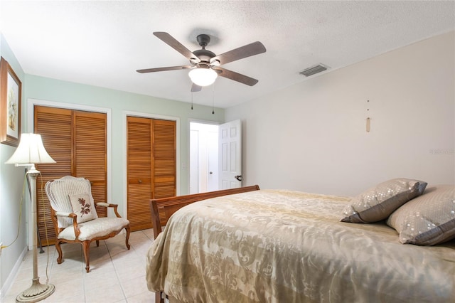 bedroom with light tile patterned floors, visible vents, a ceiling fan, a textured ceiling, and two closets