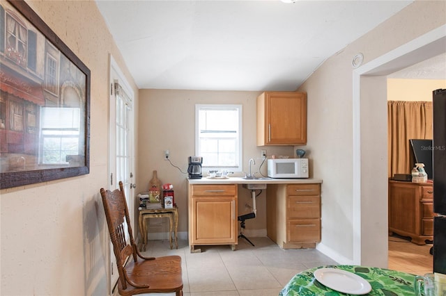 kitchen featuring light tile patterned floors, baseboards, white microwave, light countertops, and a sink