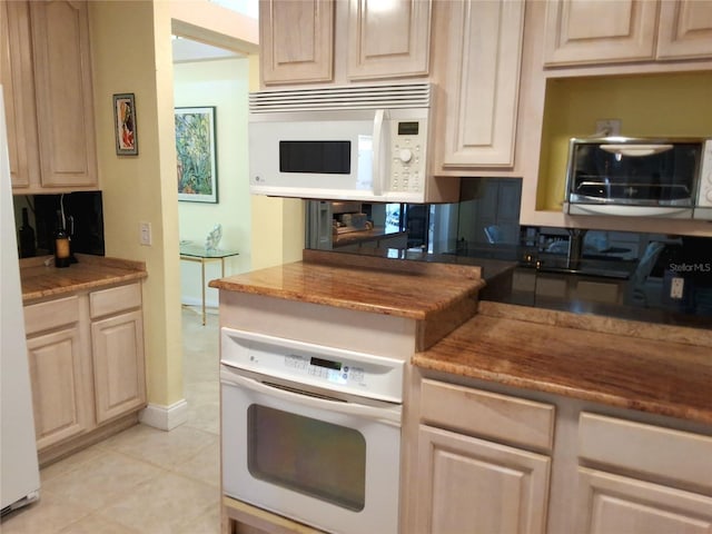 kitchen with light tile patterned floors, light brown cabinetry, white appliances, and a toaster