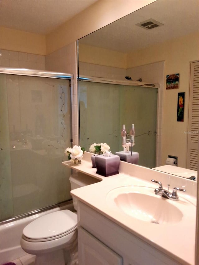 full bath with visible vents, vanity, toilet, and bath / shower combo with glass door