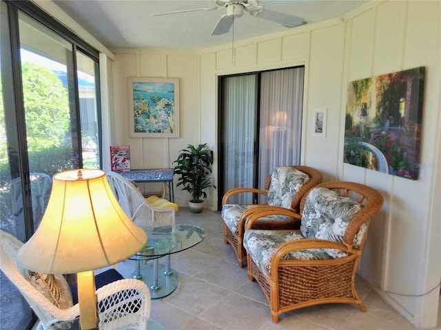 sitting room with a ceiling fan, light tile patterned flooring, and a decorative wall