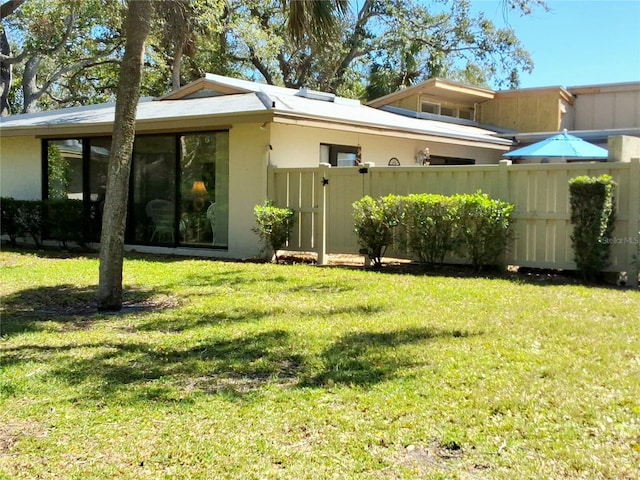 view of side of property with stucco siding, fence, and a lawn