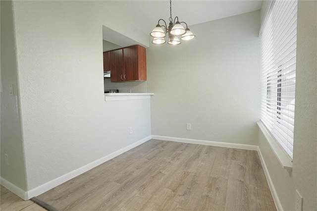 unfurnished dining area with light wood-style flooring, baseboards, and an inviting chandelier