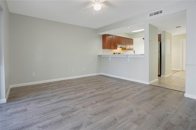 unfurnished living room with light wood-type flooring, baseboards, visible vents, and ceiling fan