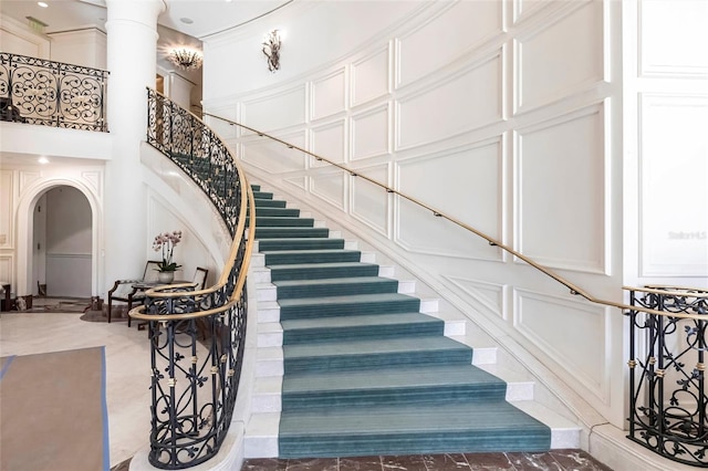 stairs featuring a high ceiling, a decorative wall, arched walkways, and ornamental molding