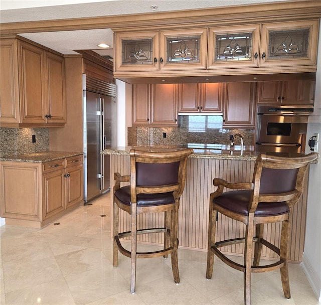 35 Watergate Dr Unit 1103, Sarasota, FL 34236 - kitchen with stainless steel appliances, a breakfast bar, tasteful backsplash, dark stone countertops, and brown cabinetry