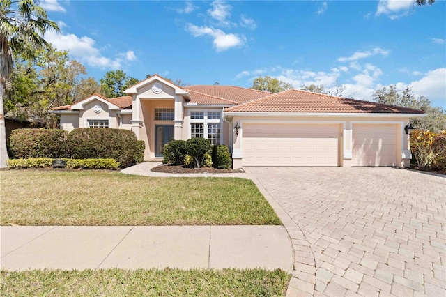 mediterranean / spanish-style house with a garage, a tiled roof, decorative driveway, a front lawn, and stucco siding