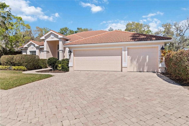 mediterranean / spanish house with a garage, decorative driveway, a tile roof, and stucco siding