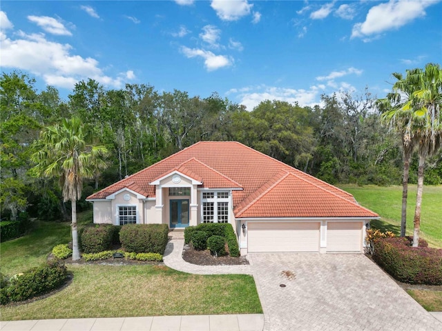 mediterranean / spanish house with a tiled roof, decorative driveway, a front yard, and stucco siding