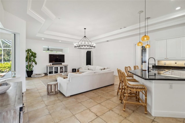 living room featuring a chandelier, a raised ceiling, crown molding, and recessed lighting