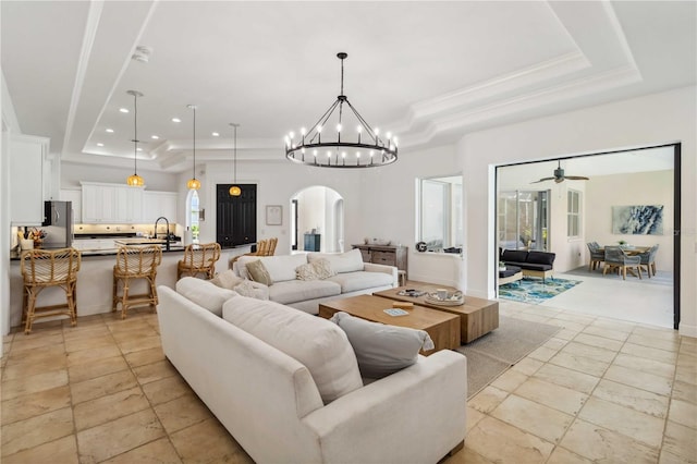 living area with arched walkways, ornamental molding, ceiling fan with notable chandelier, a tray ceiling, and recessed lighting