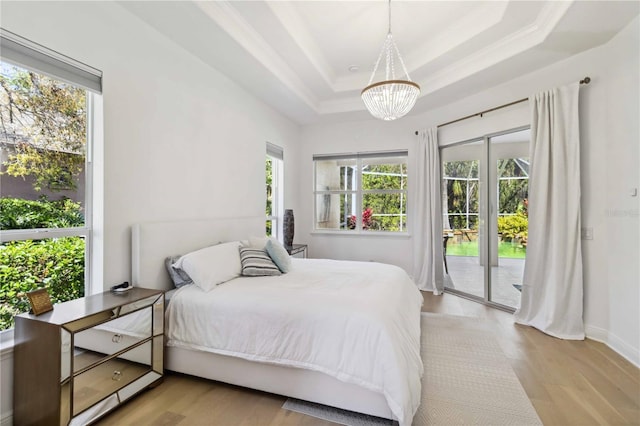 bedroom with access to exterior, a tray ceiling, light wood-type flooring, and ornamental molding