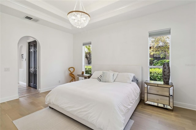 bedroom with a tray ceiling, arched walkways, visible vents, wood finished floors, and baseboards