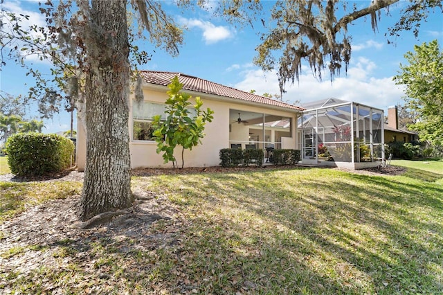 exterior space with ceiling fan, a lanai, a tiled roof, a lawn, and stucco siding