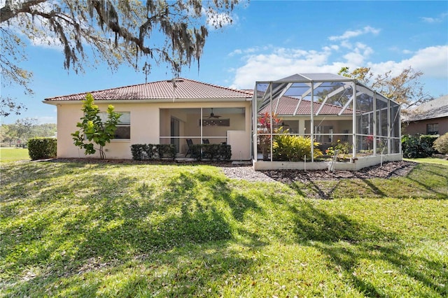 back of house featuring a lanai, a tile roof, a ceiling fan, a yard, and stucco siding