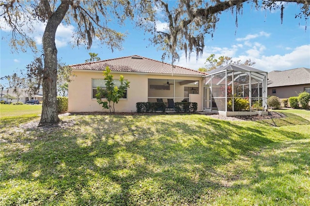 back of house featuring a lawn, ceiling fan, a tiled roof, a lanai, and stucco siding