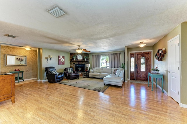 living area with visible vents, a fireplace, a textured ceiling, and light wood-style floors