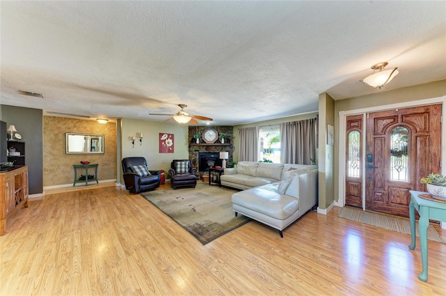 living area with visible vents, a fireplace, a textured ceiling, and light wood-type flooring