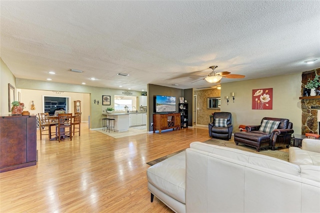 living room featuring a stone fireplace, light wood-style flooring, visible vents, and a textured ceiling