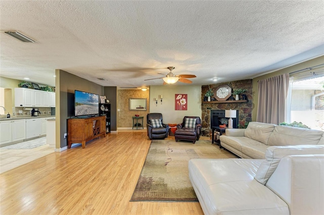 living area with visible vents, a fireplace, ceiling fan, a textured ceiling, and light wood-type flooring