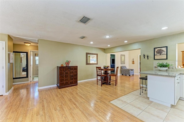 kitchen featuring light wood finished floors, visible vents, a breakfast bar, white cabinets, and a textured ceiling